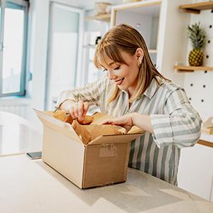 A smiling blonde woman with a striped shirt opens up a package. 